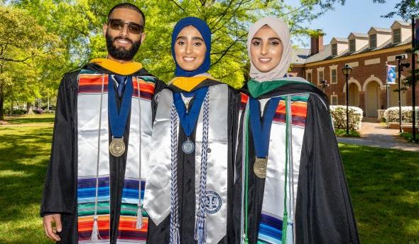 Sana, Seena and Fozi Alkaifi pose in graduation regalia with Rollins Hall in the background.