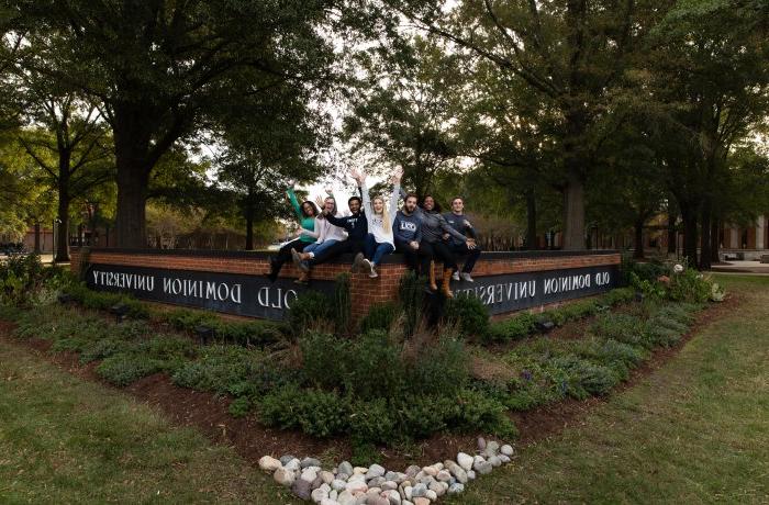 A group of students sit on the Old Dominion University sign.